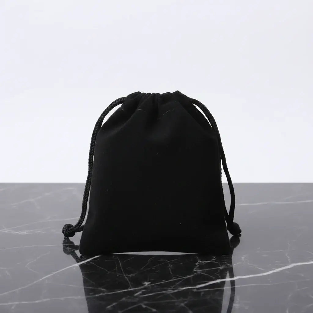 Black drawstring pouch for jewelry or gift packaging on marble surface.
